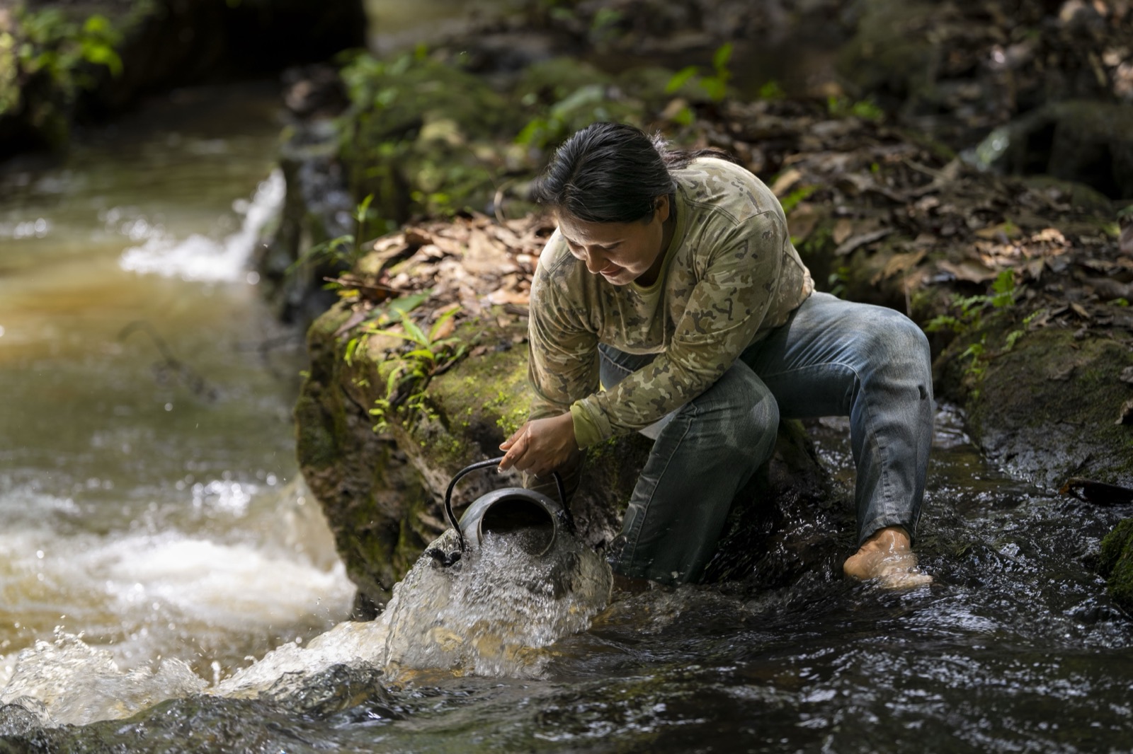 Woman collecting water from stream in forest